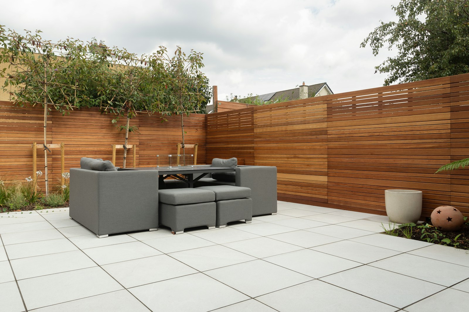 Terras van lichte keramische tegels met loungeset en houten schutting