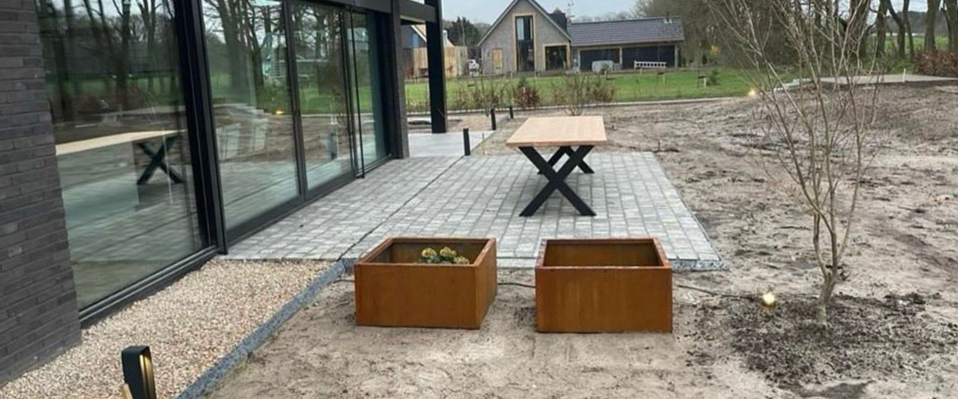 Tuin in renovatie bij een moderne woning met nieuwe bestrating en cortenstalen plantenbakken